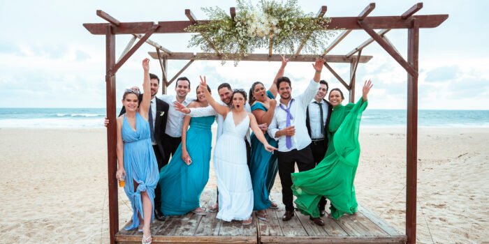Casamento na Igreja São João Eudes: Jéssica e Ramiro erguem os braços com os convidados na praia.