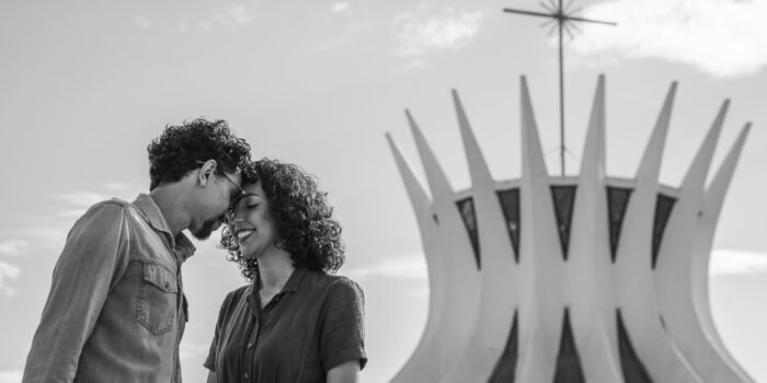 Em preto e branco, Anna e Francisco encostam a testa, com a cruz da catedral ao fundo.