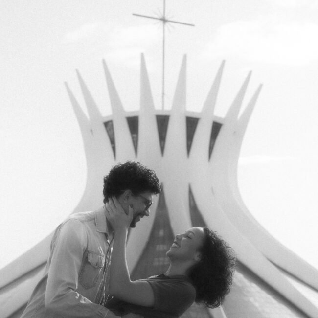 Francisco segura Anna inclinada, a mão dela no rosto dele, com a catedral atrás.