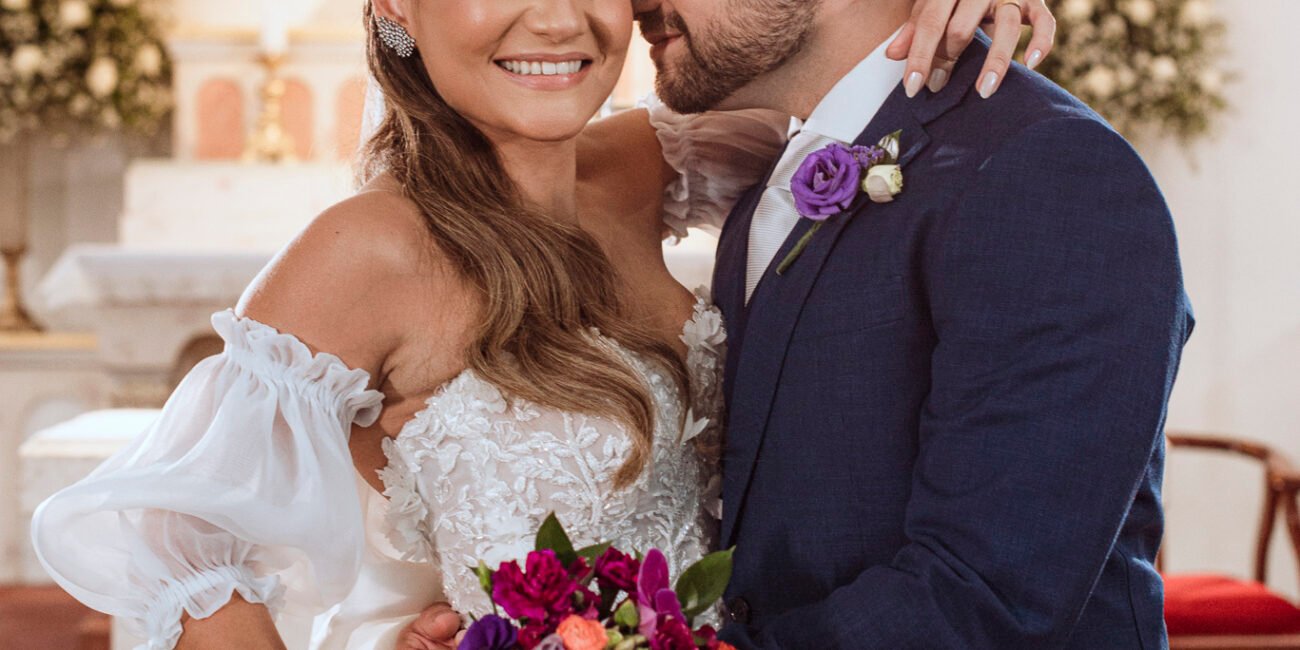 Casal sorrindo abraçado, com o buquê colorido de Ana