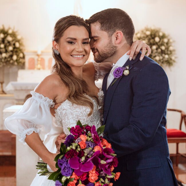 Casal sorrindo abraçado, com o buquê colorido de Ana
