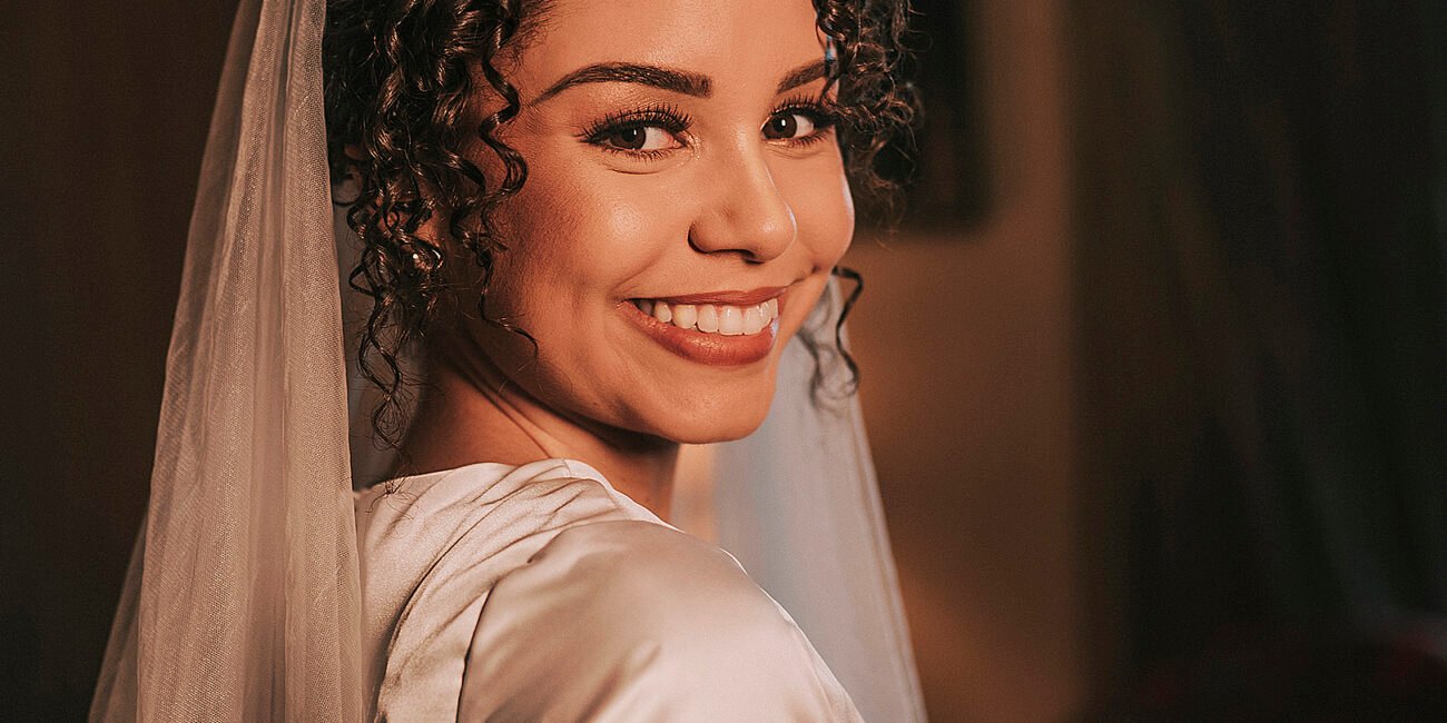 Ana Lídia sorri por cima do ombro, de tiara e véu.