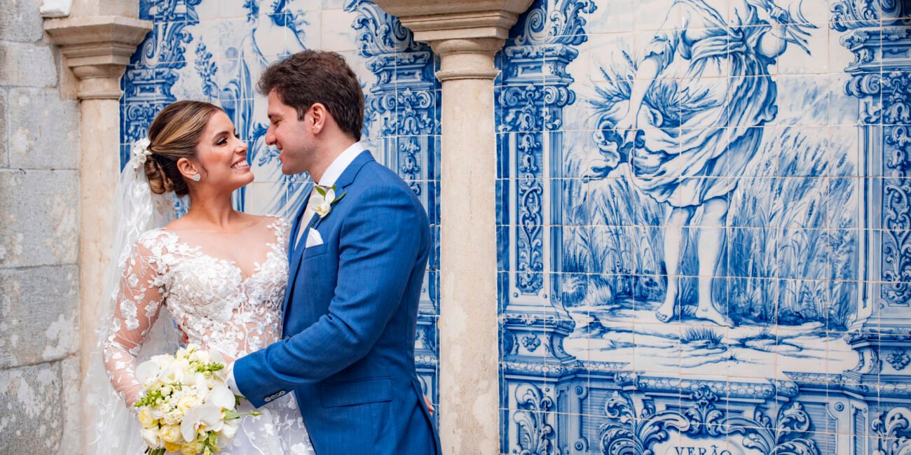 Bia e Márcio se olham diante de um painel de azulejos azuis.