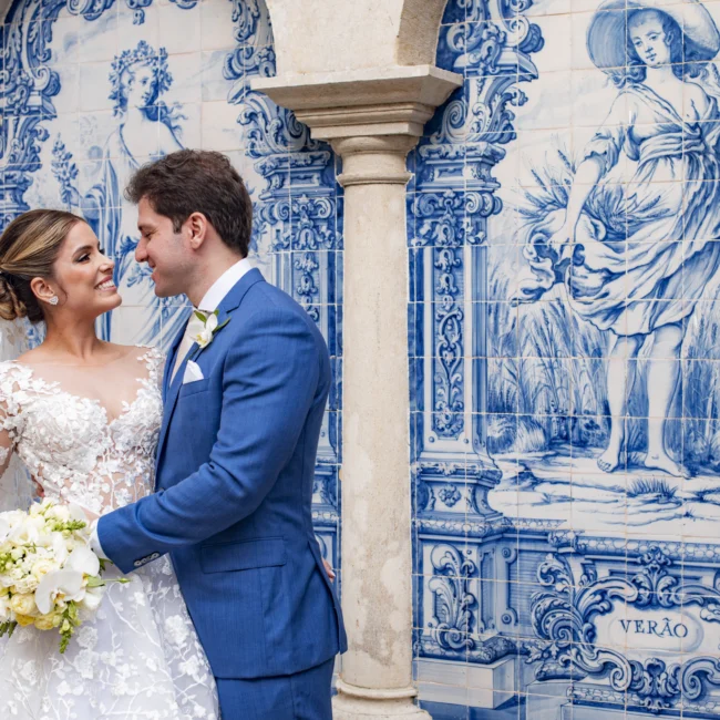 Bia e Márcio se olham diante de um painel de azulejos azuis.