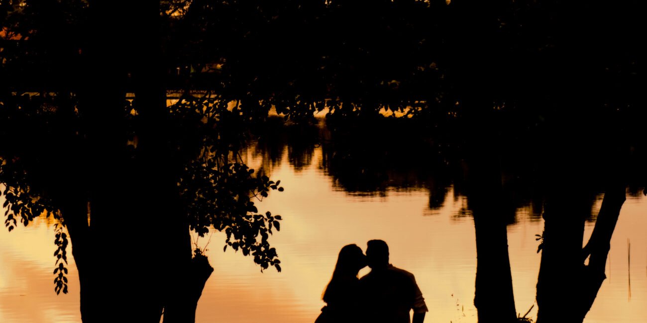Evellyne e Rafael em silhueta diante do lago durante o pôr do sol em Guaramiranga