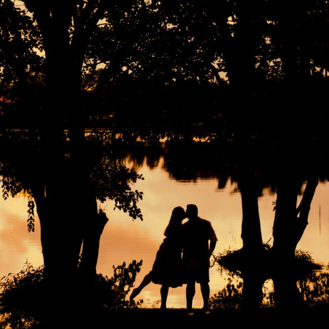Evellyne e Rafael em silhueta diante do lago durante o pôr do sol em Guaramiranga