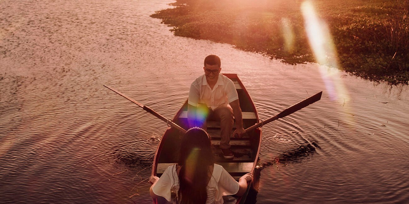 Thiago rema e Raquel está de costas, os dois de branco no barco.